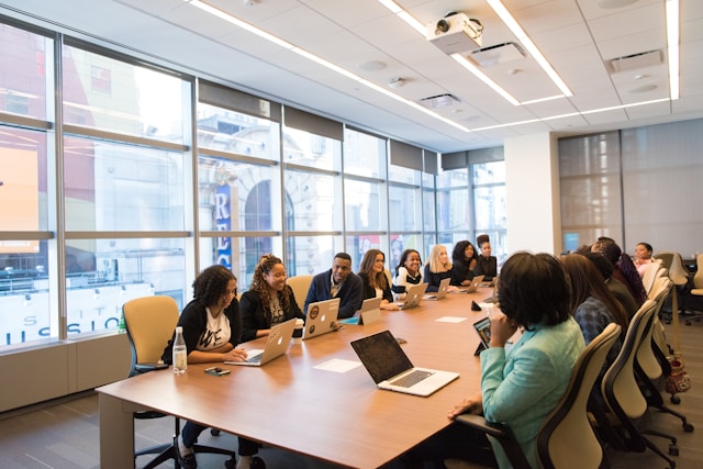 group-of-people-sitting-beside-rectangular-wooden-table-with-laptops